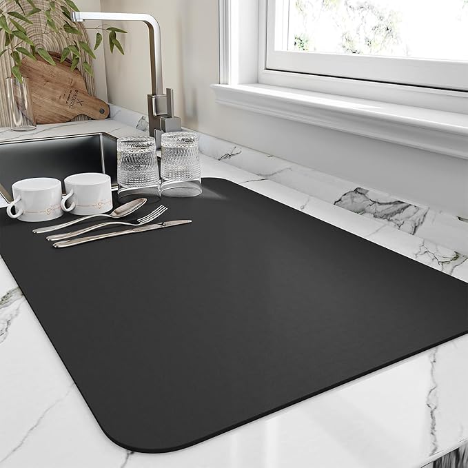 Black dish drying mat on a marble counter with cups, glasses and cutlery